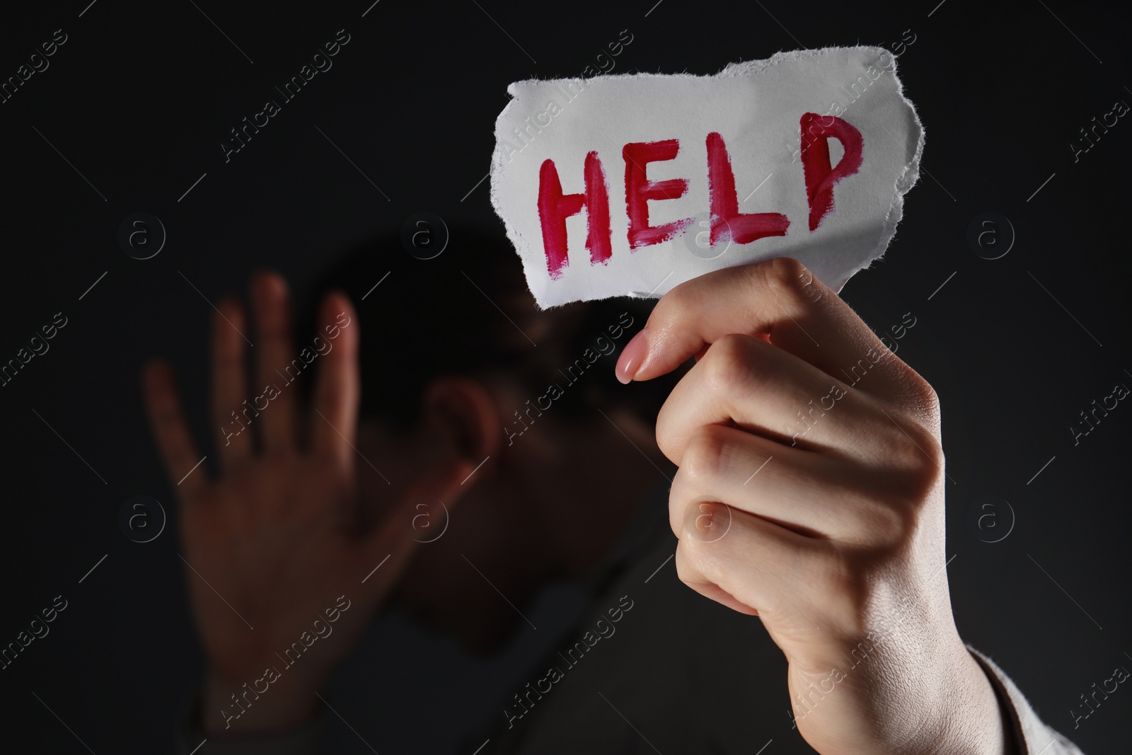 Photo of Woman holding piece of paper with word Help on black background, closeup. Domestic violence concept