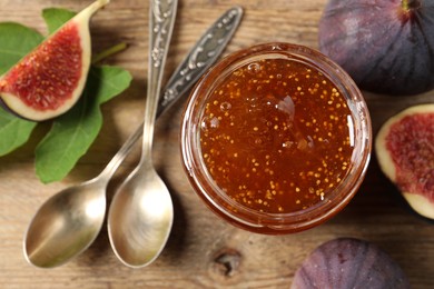 Photo of Glass jar with tasty sweet jam, spoons and fresh figs on wooden table, flat lay