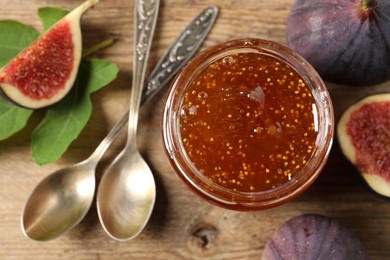 Glass jar with tasty sweet jam, spoons and fresh figs on wooden table, flat lay