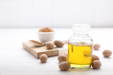 Bottle of nutmeg oil and nuts on white wooden table, space for text