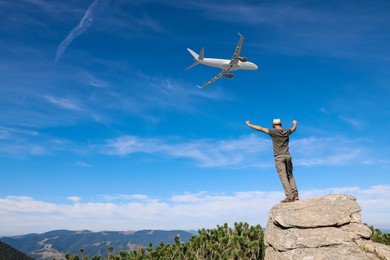 Image of Man on cliff looking at airplane flying in sky