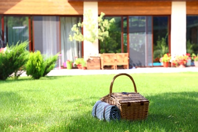 Picnic basket with blanket on green lawn in garden. Space for text