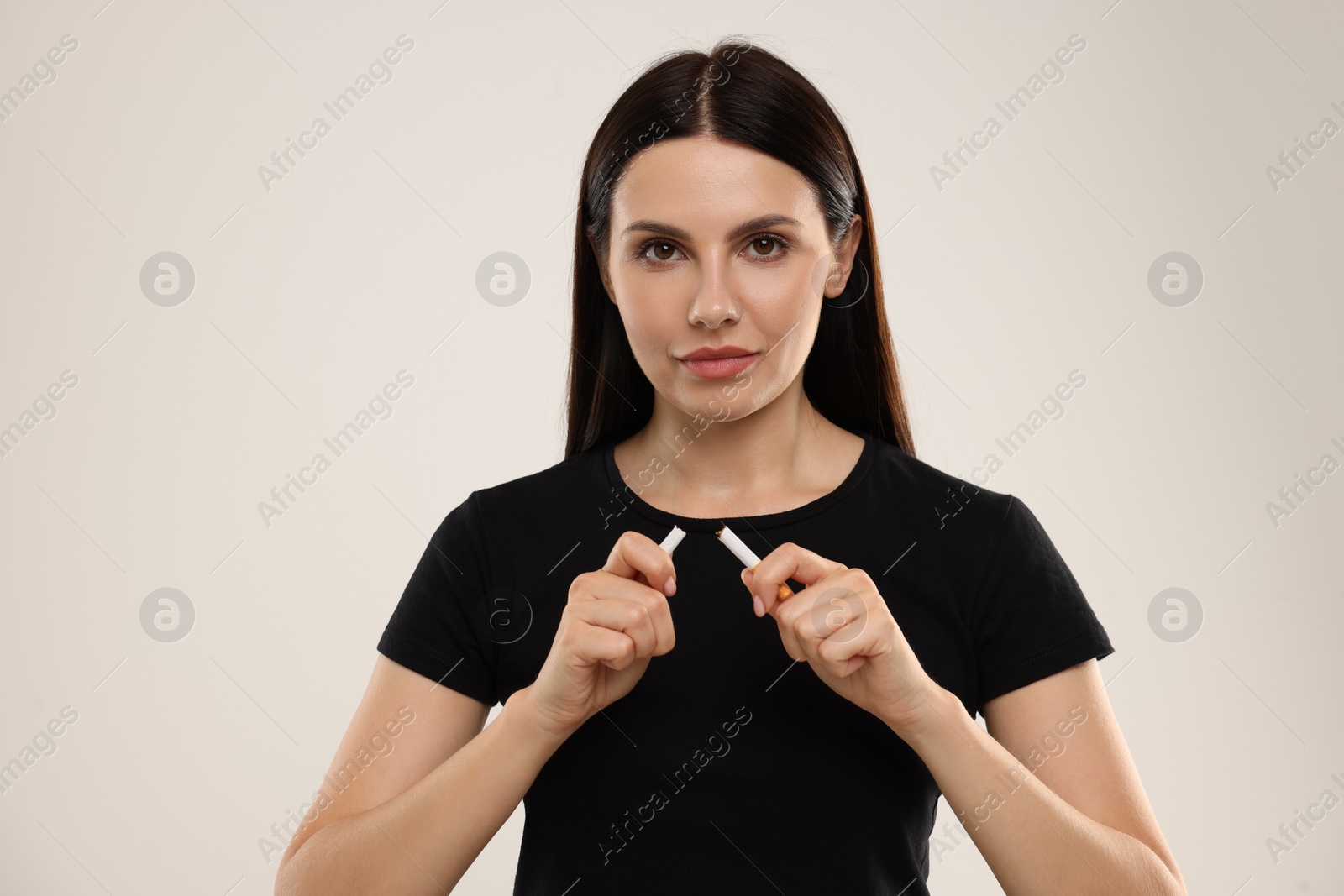 Photo of Stop smoking concept. Woman breaking cigarette on beige background