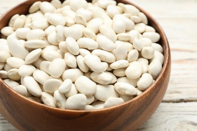 Bowl of uncooked white beans on wooden table, closeup