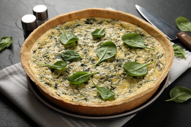 Photo of Delicious homemade spinach pie, spices and knife on black table