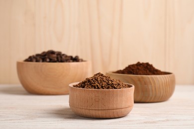 Bowls with different types of coffee on white wooden table