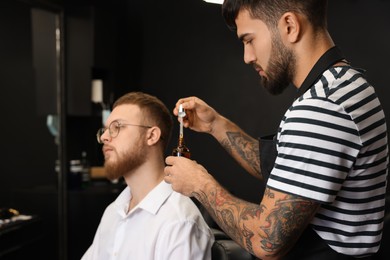 Photo of Hairdresser with beard oil near client in barbershop. Professional shaving service