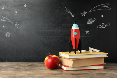 Photo of Bright toy rocket and school supplies on wooden desk. Space for text