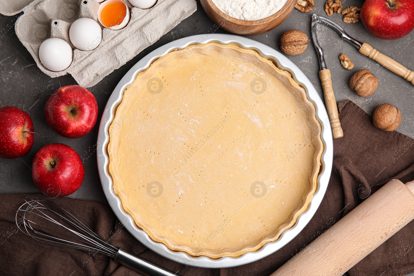 Photo of Raw dough and ingredients for traditional English apple pie on grey table, flat lay