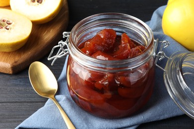 Quince jam in glass jar, spoon and fresh raw fruits on grey table, closeup