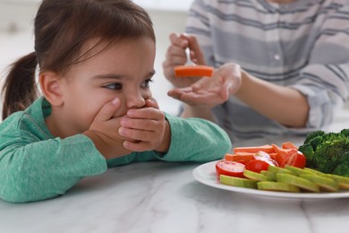 Mother feeding her daughter indoors, closeup. Little girl refusing to eat vegetables