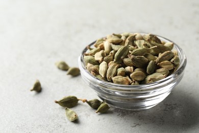 Glass bowl of dry cardamom pods on light grey table
