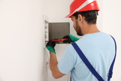 Electrician installing fuse box with screwdriver indoors