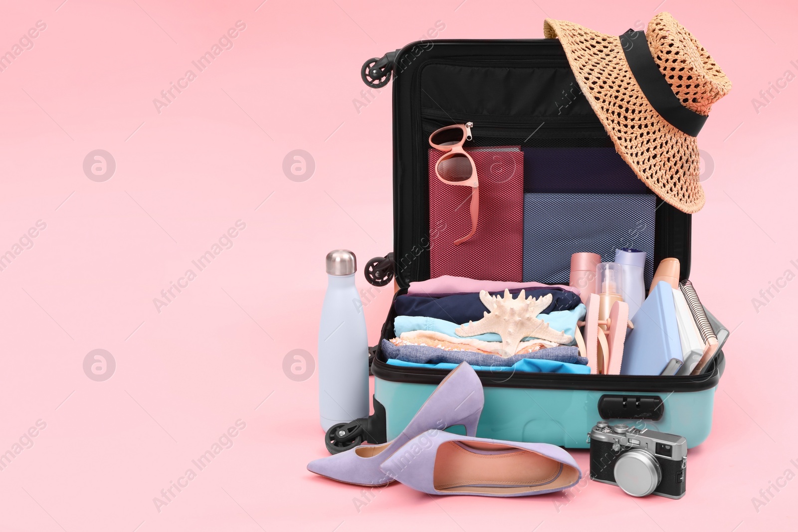 Photo of Open suitcase with clothes, beach accessories and shoes on pink background, space for text. Summer vacation