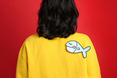 Woman with paper fish on back against red background. April fool's day