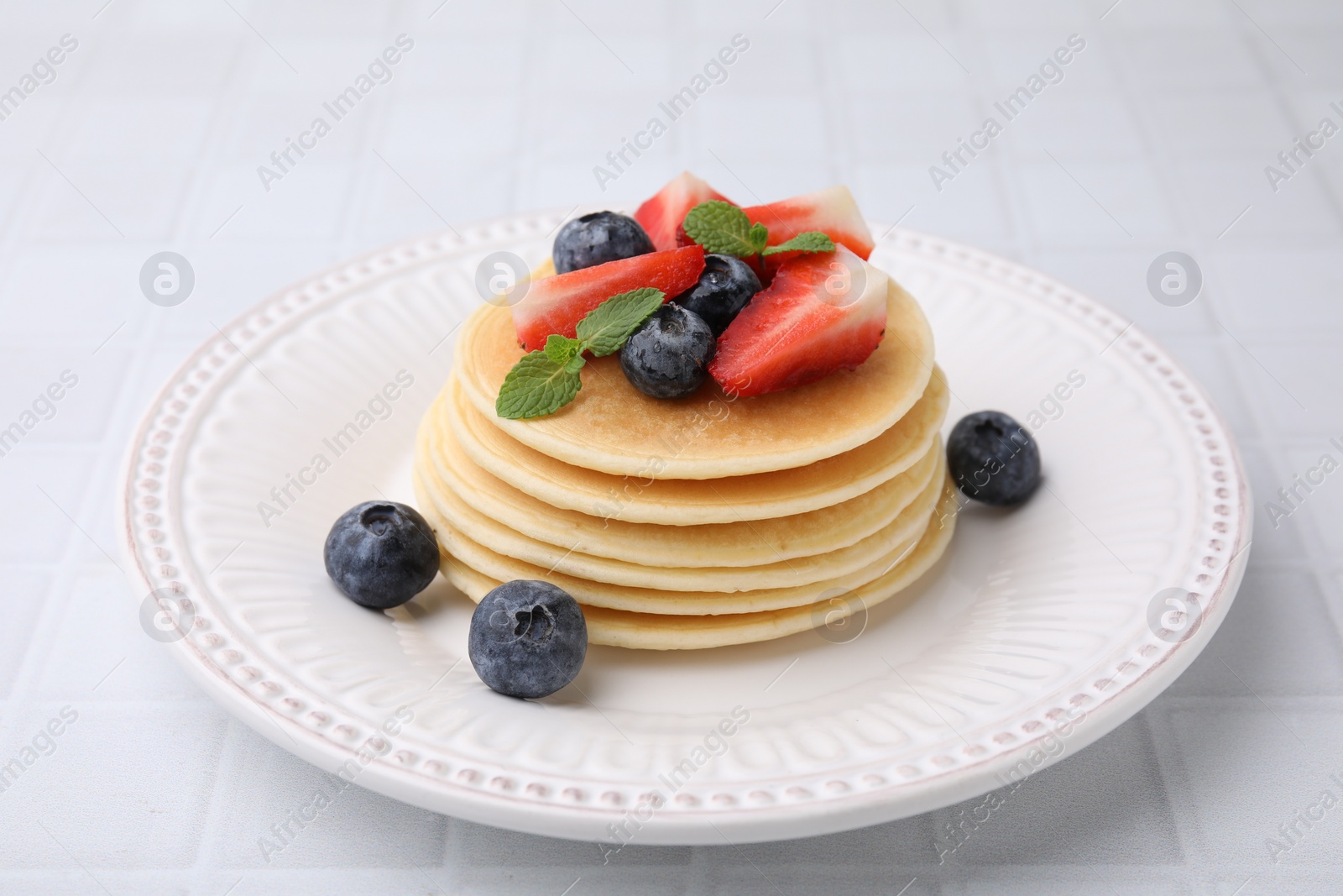 Photo of Delicious pancakes with strawberries, blueberries and mint on white tiled table, closeup