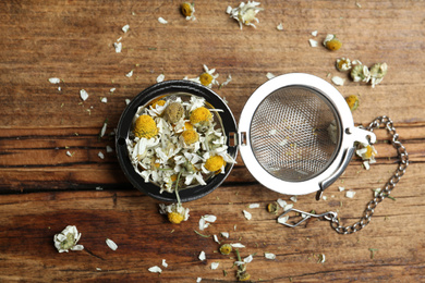 Photo of Dry chamomile flowers in infuser on wooden table, flat lay