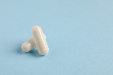 Photo of Two white pills on light blue background, closeup. Space for text