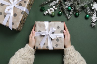 Photo of Christmas present. Woman with gift boxes, fir tree branches and festive decor on dark green background, top view