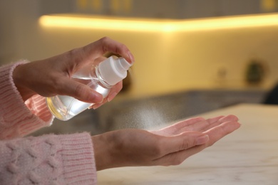 Photo of Woman spraying antiseptic onto hand against blurred background, closeup