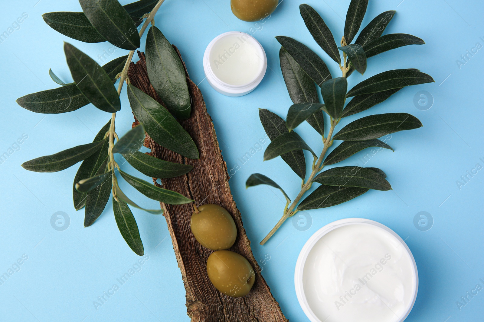 Photo of Flat lay composition with jars of cream and olives on light blue background