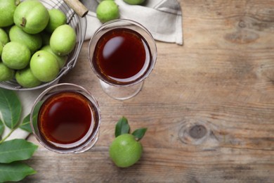 Photo of Delicious liqueur and green walnuts on wooden table, flat lay. Space for text