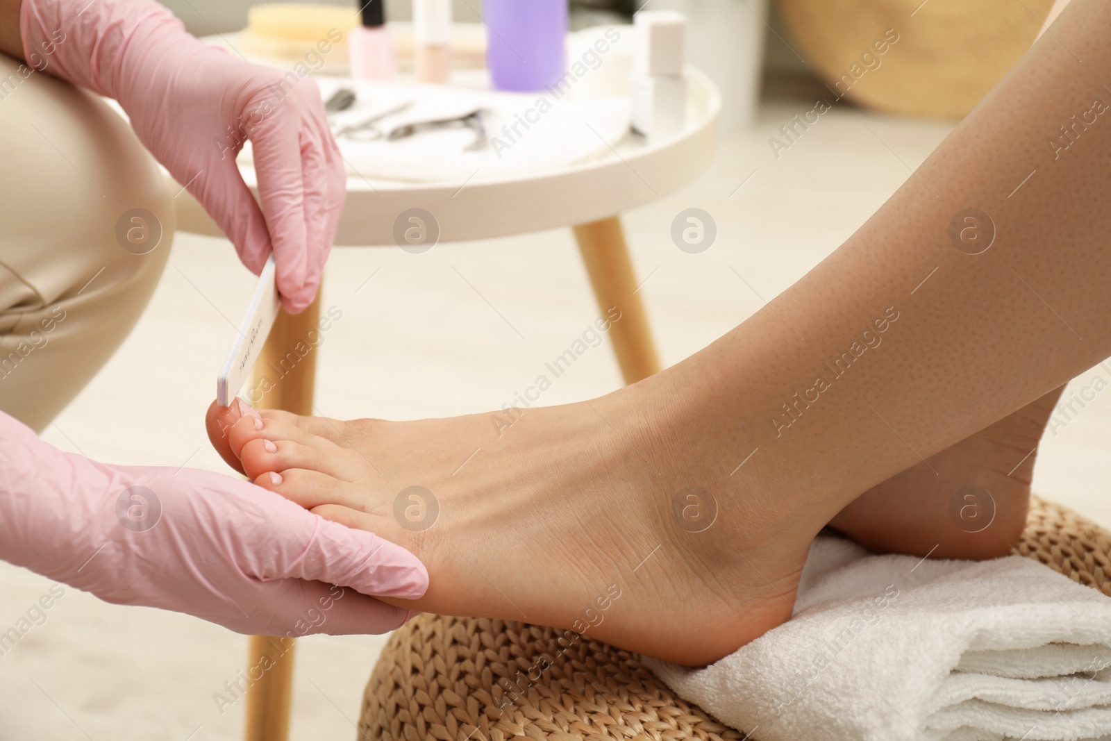 Photo of Professional pedicurist filing client`s toenails in beauty salon, closeup