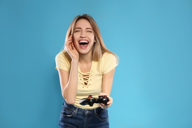 Emotional young woman playing video games with controller on color background. Space for text