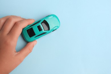 Photo of Child playing with toy car on light blue background, top view. Space for text