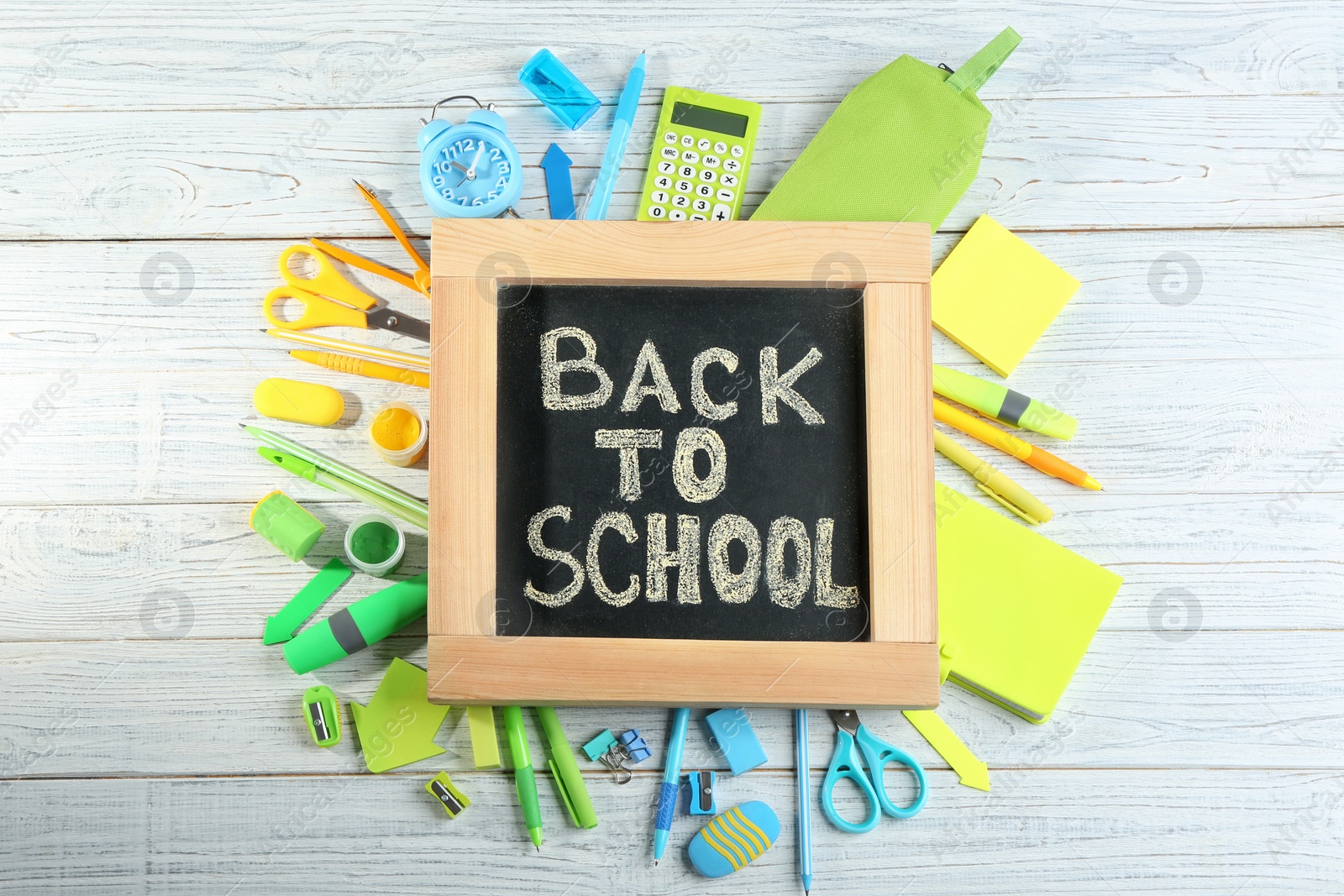 Photo of Chalkboard with phrase "BACK TO SCHOOL" and different stationery on white wooden background, flat lay
