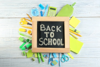Chalkboard with phrase "BACK TO SCHOOL" and different stationery on white wooden background, flat lay