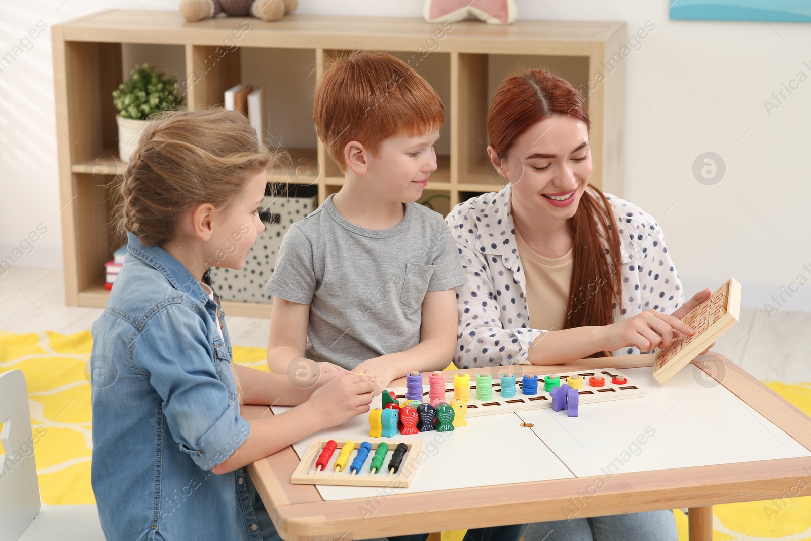 Photo of Happy mother and children playing with different math game kits at desk in room. Study mathematics with pleasure