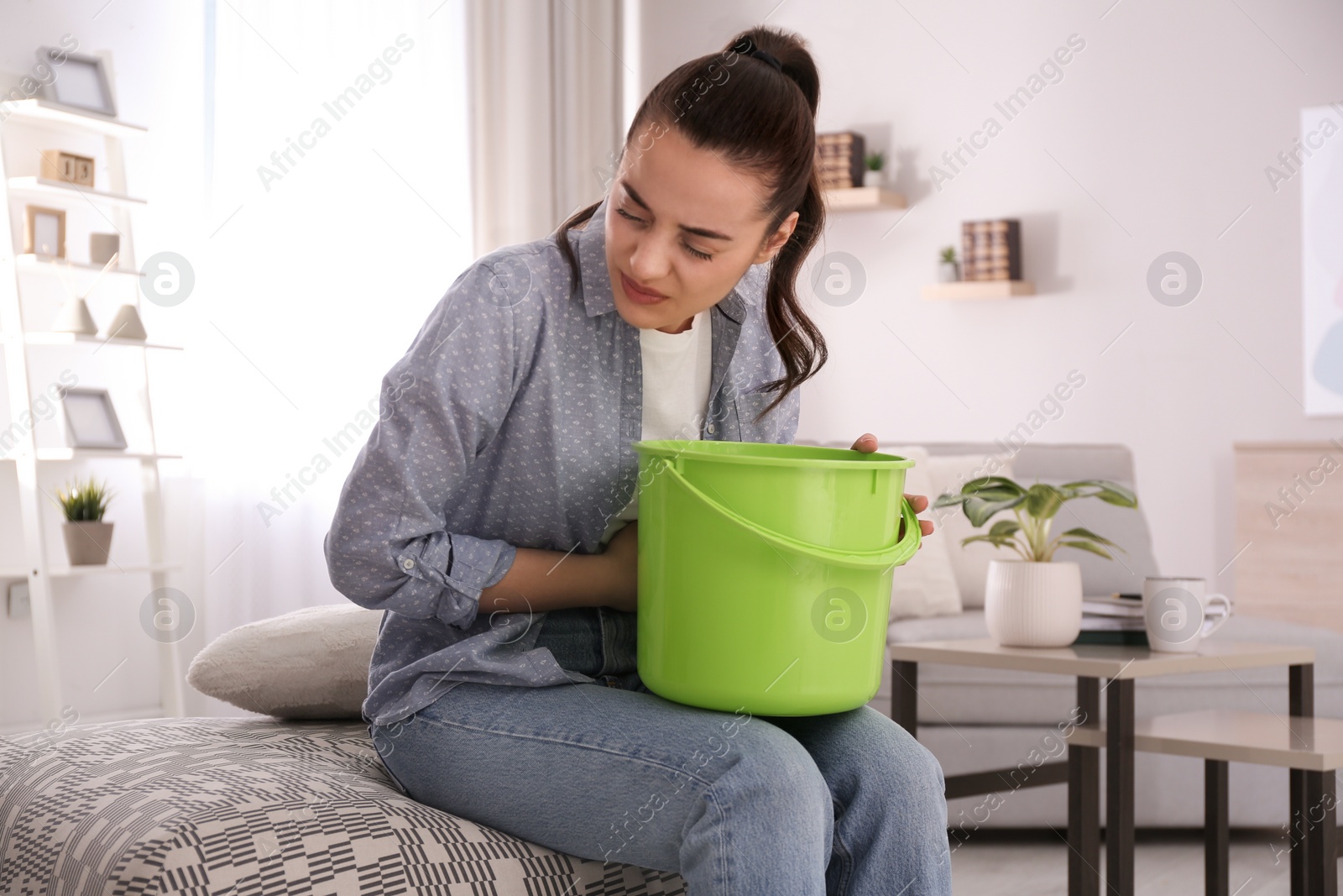 Photo of Young woman with bucket suffering from nausea at home. Food poisoning