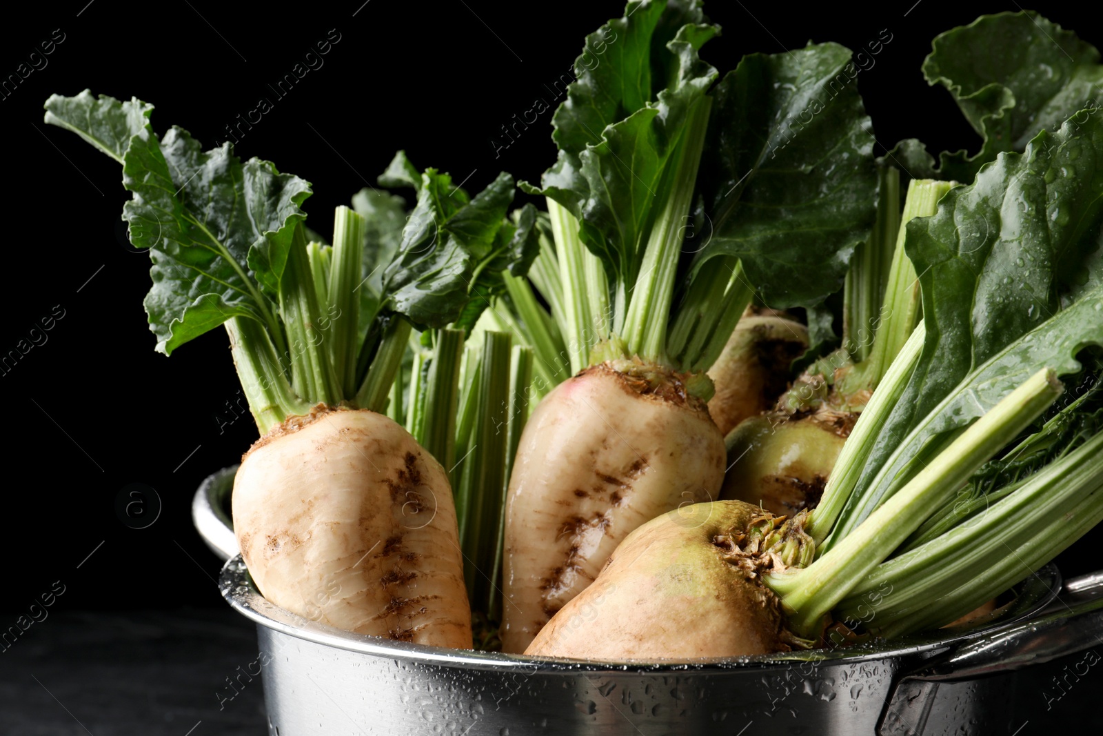 Photo of Colander with fresh sugar beets on black table, closeup