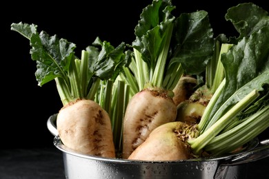 Photo of Colander with fresh sugar beets on black table, closeup
