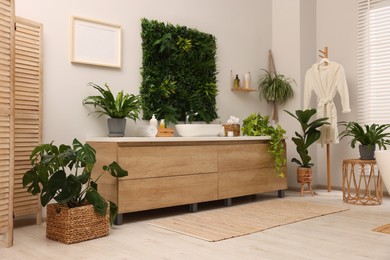 Green artificial plants, vanity and different personal care products in bathroom