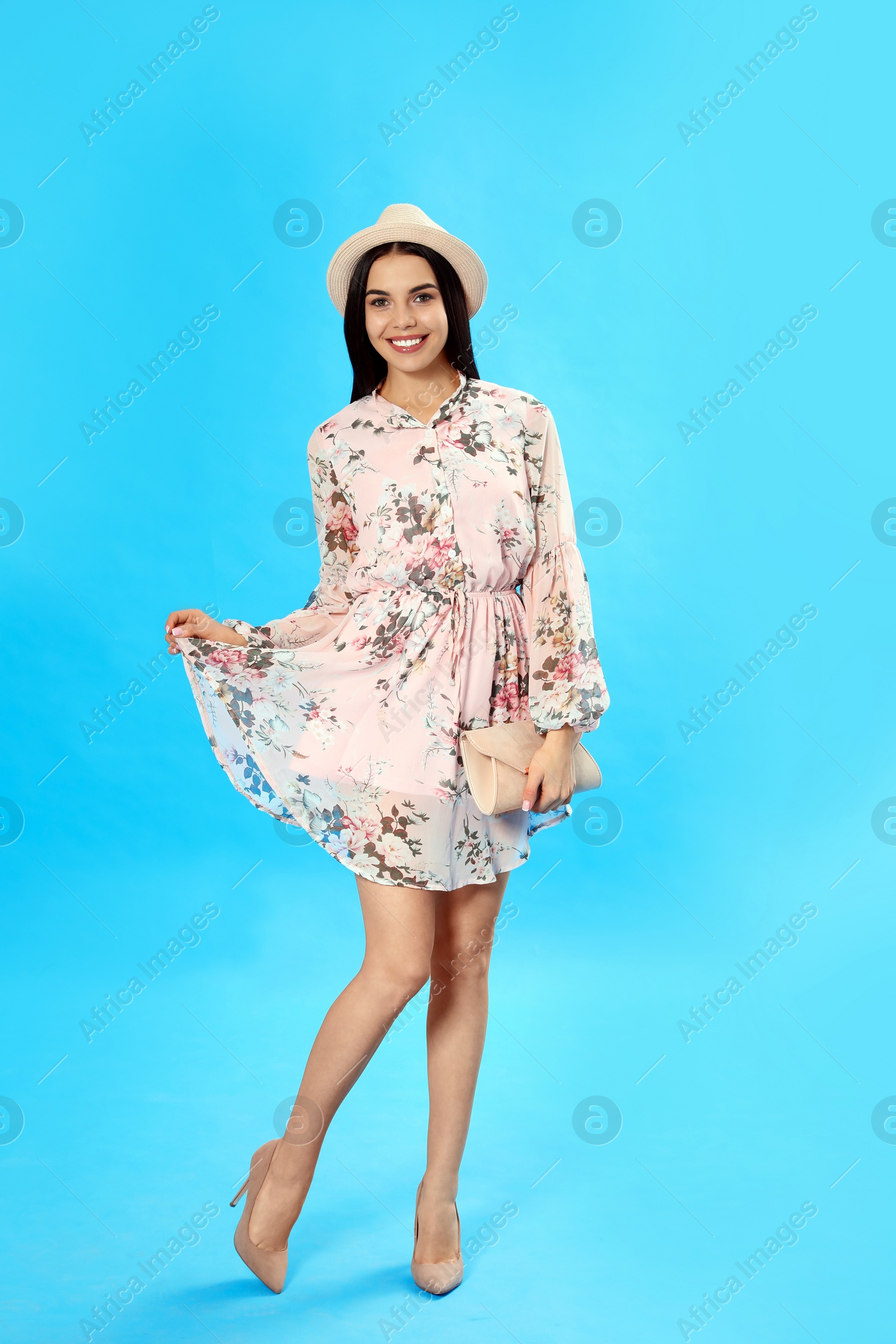 Photo of Young woman wearing floral print dress with clutch on light blue background