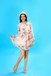 Photo of Young woman wearing floral print dress with clutch on light blue background