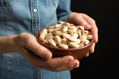 Photo of Woman holding bowl with pistachio nuts on black background, closeup