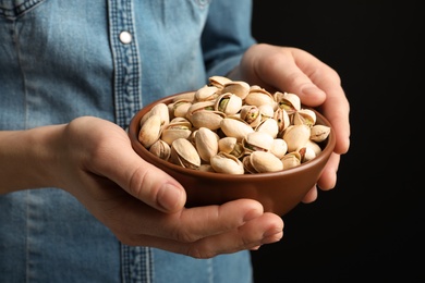 Woman holding bowl with pistachio nuts on black background, closeup