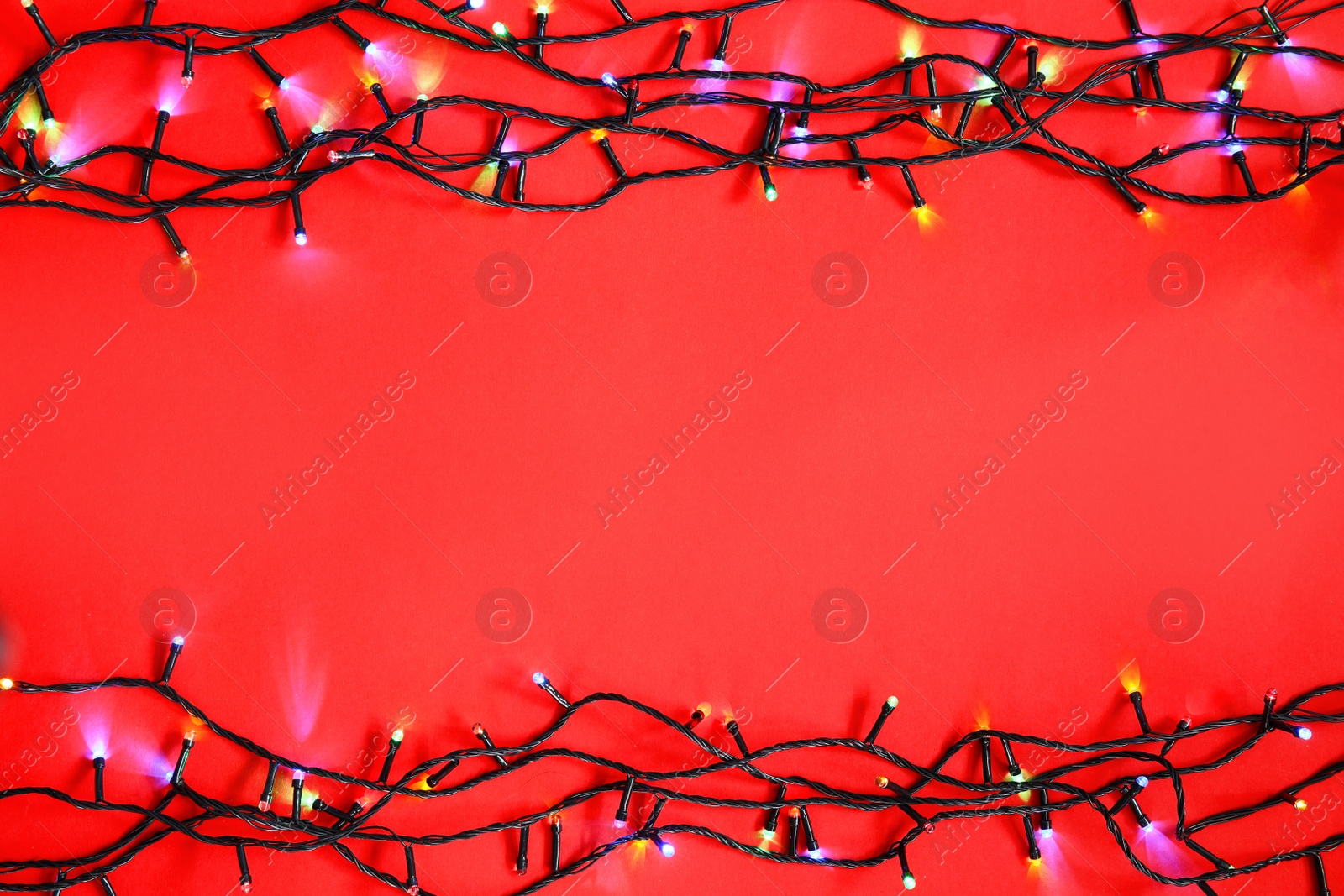 Photo of Glowing Christmas lights on color background, top view