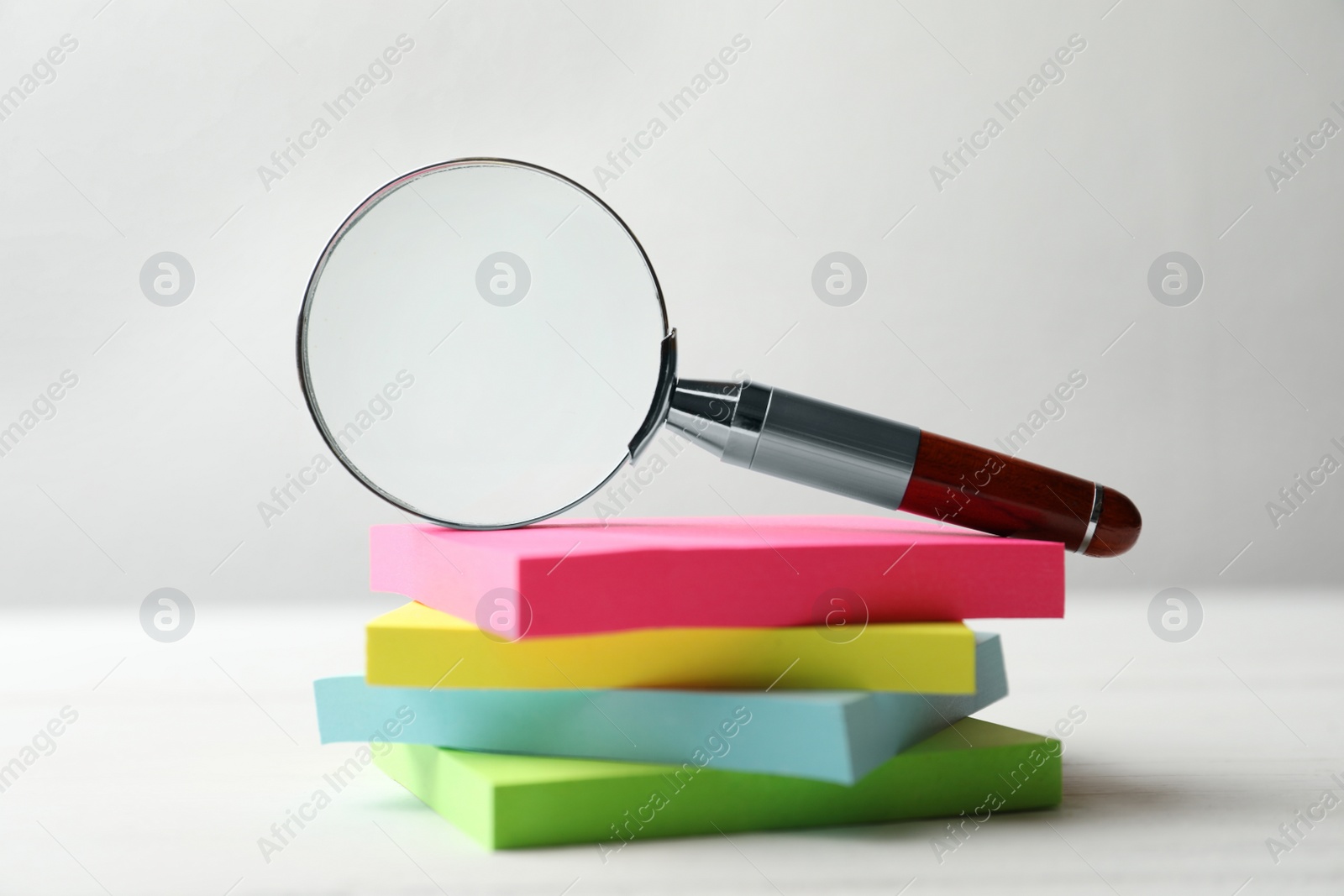 Photo of Magnifier glass and stack of colorful memory stickers on white table, closeup. Find keywords concept