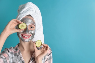 Photo of Young woman with cleansing mask on her face holding cucumber slices against color background, space for text. Skin care