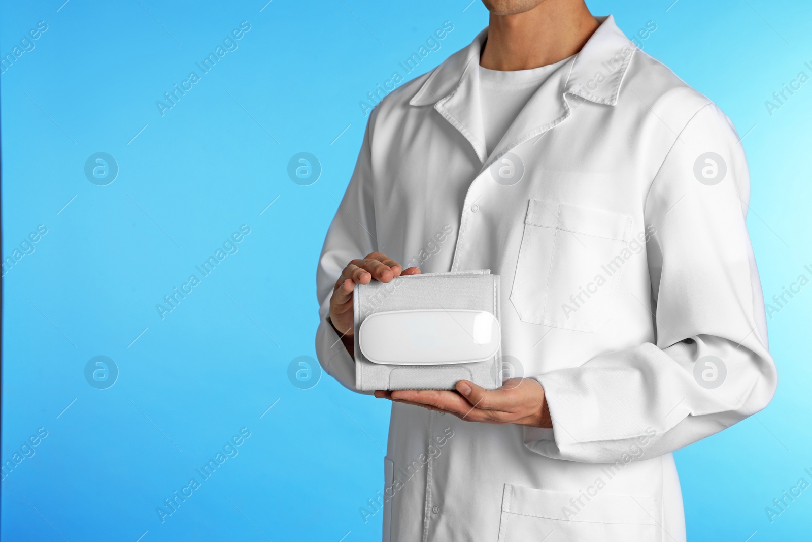 Photo of Male doctor holding blood pressure meter on color background, closeup with space for text. Medical object