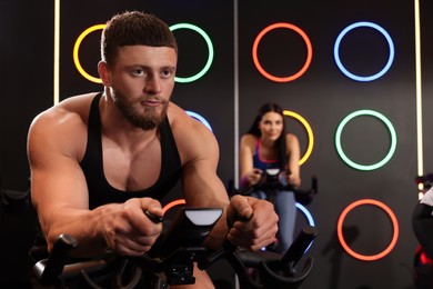 Photo of Young man and woman training on exercise bikes in fitness club