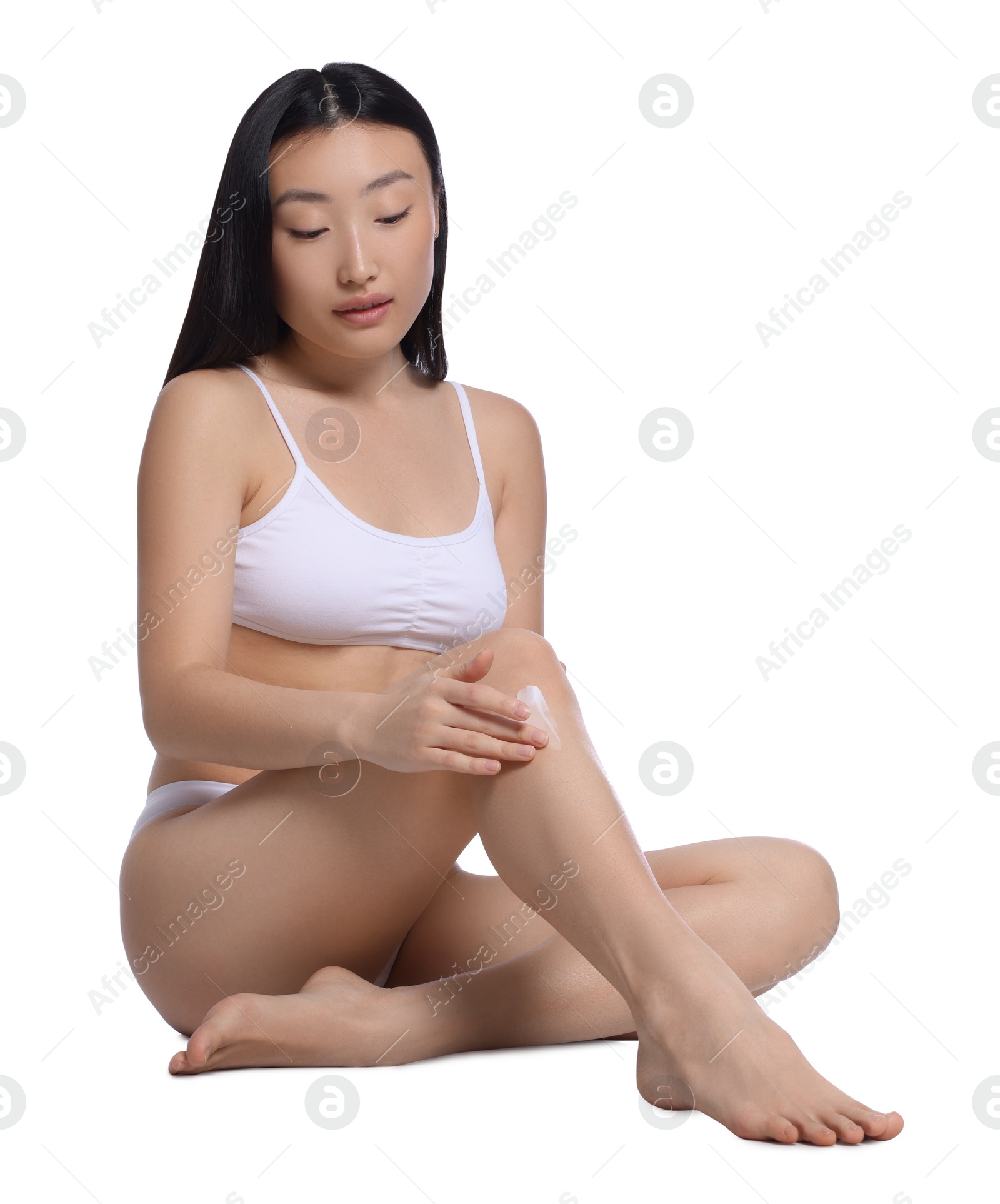 Photo of Beautiful young Asian woman applying body cream onto leg on white background