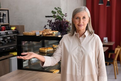 Photo of Smiling business owner inviting to come into her cafe