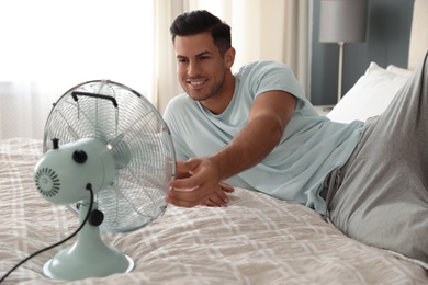 Man enjoying air flow from fan on bed in room. Summer heat