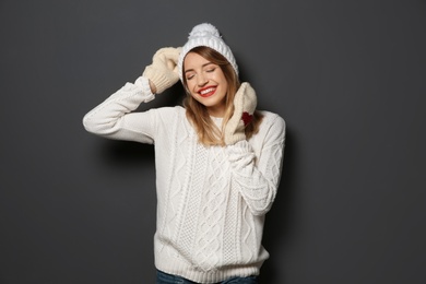 Photo of Beautiful young woman in warm sweater with hat and mittens on dark background