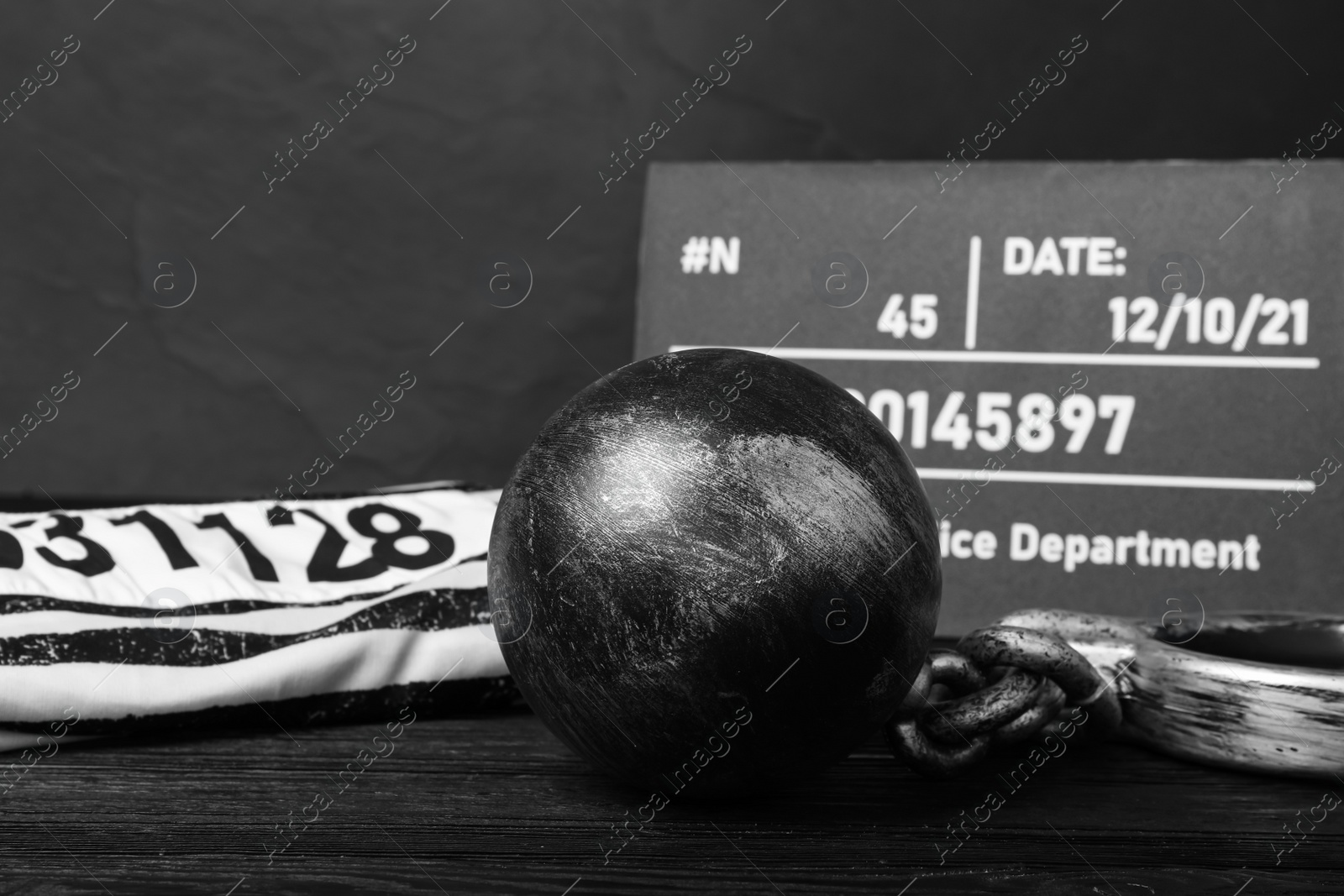 Photo of Metal ball with chain, prison uniform and mugshot letter board on black wooden table